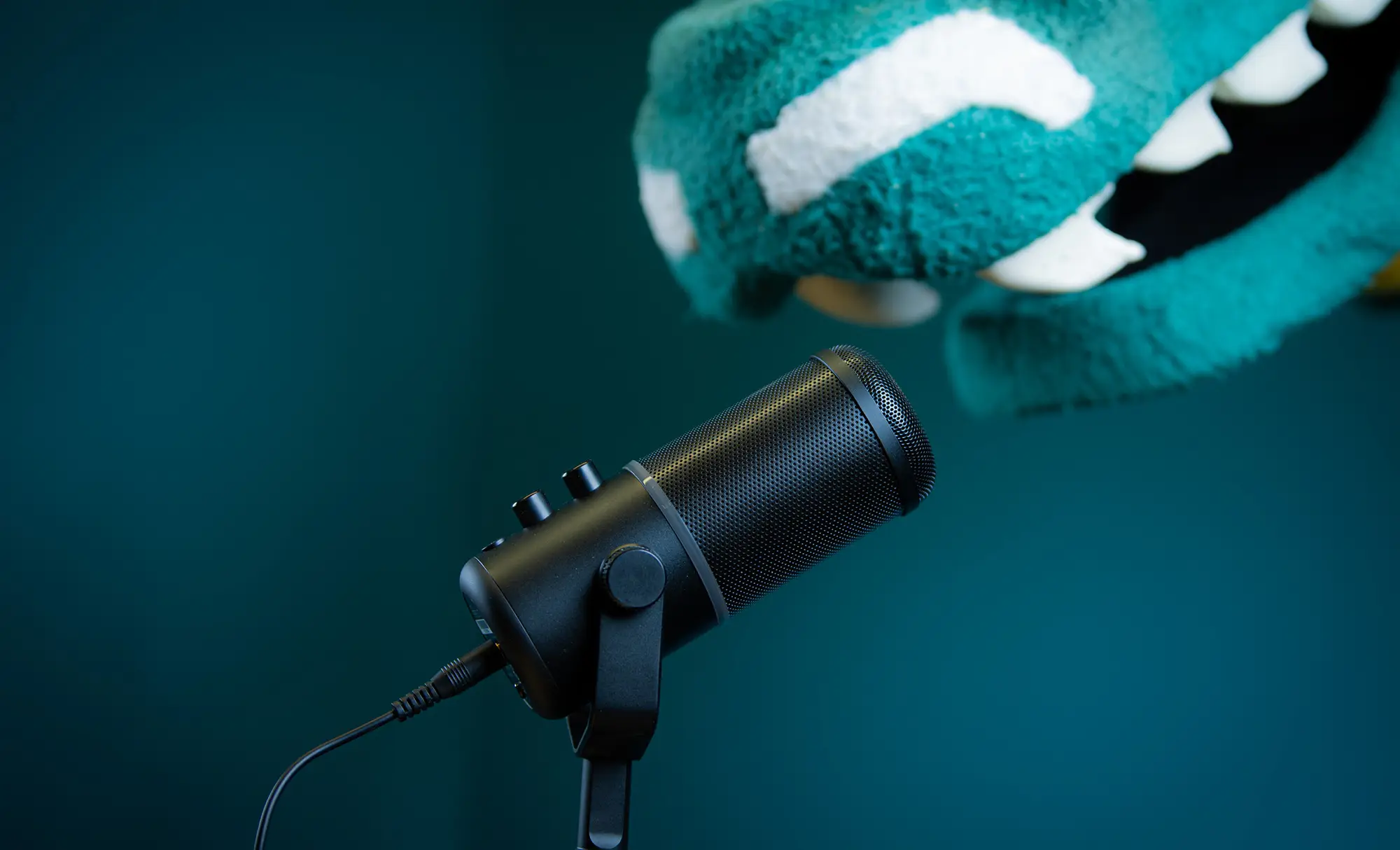 Microphone with teal background and snout of Seawolf mascot leaning in looking as if to speak