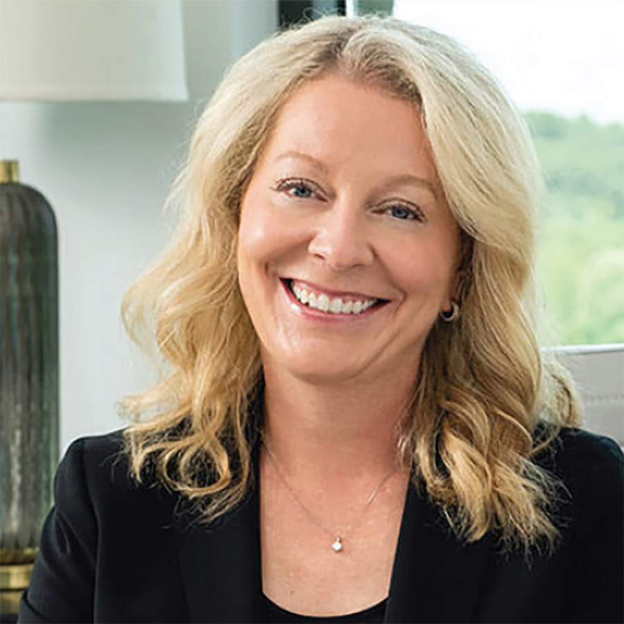 A portrait headshot photograph of Wendy Barnes smiling in a black suit and black dress shirt
