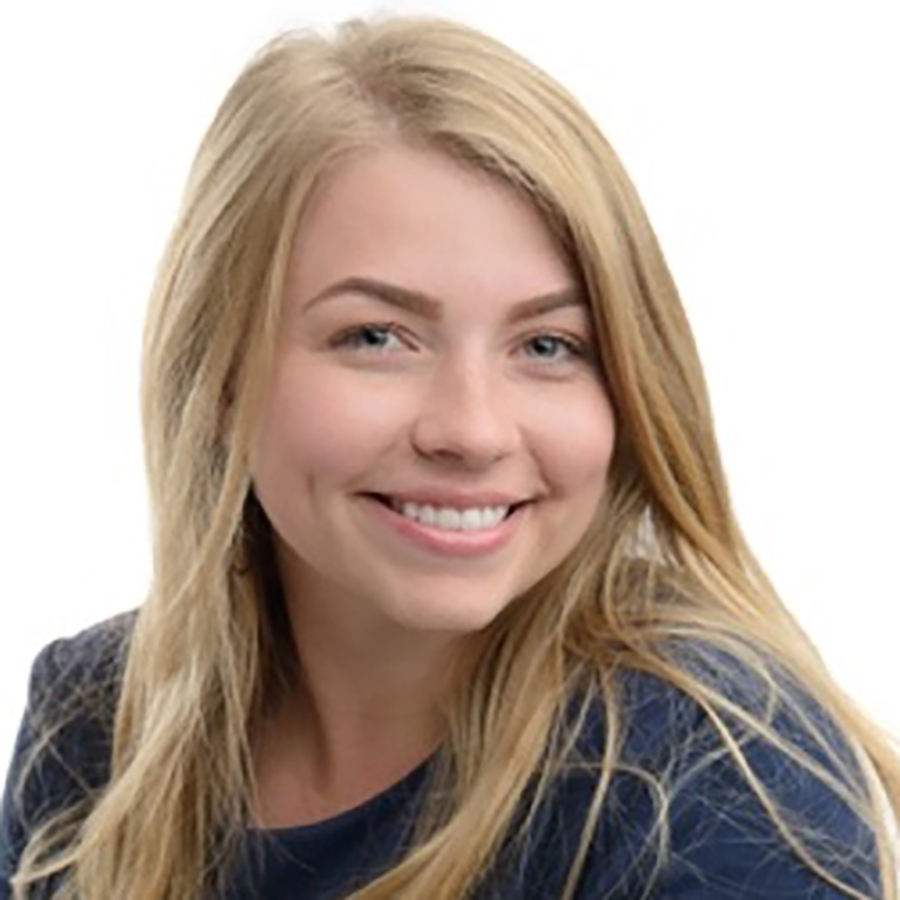 A headshot portrait picture of Kailee Stickler smiling in a dark navy blue long-sleeve t-shirt posing in front of an all white studio background