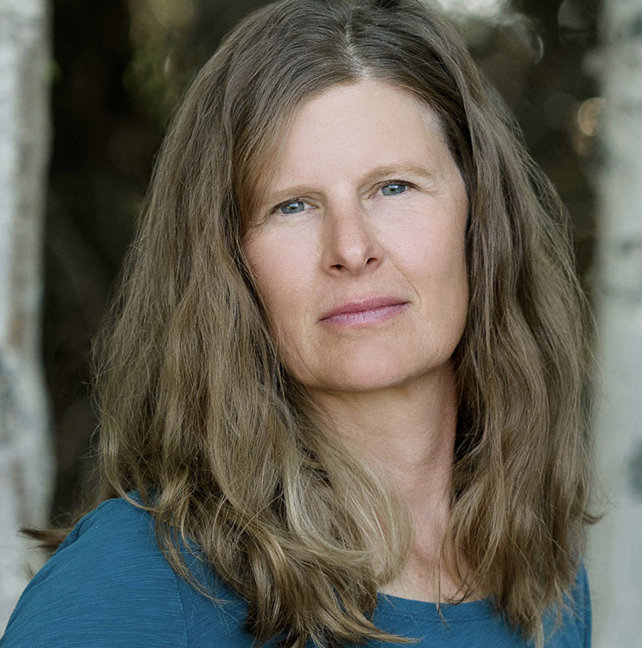 Portrait orientation close-up headshot photograph of Christine Byl grinning in a dark blue blouse