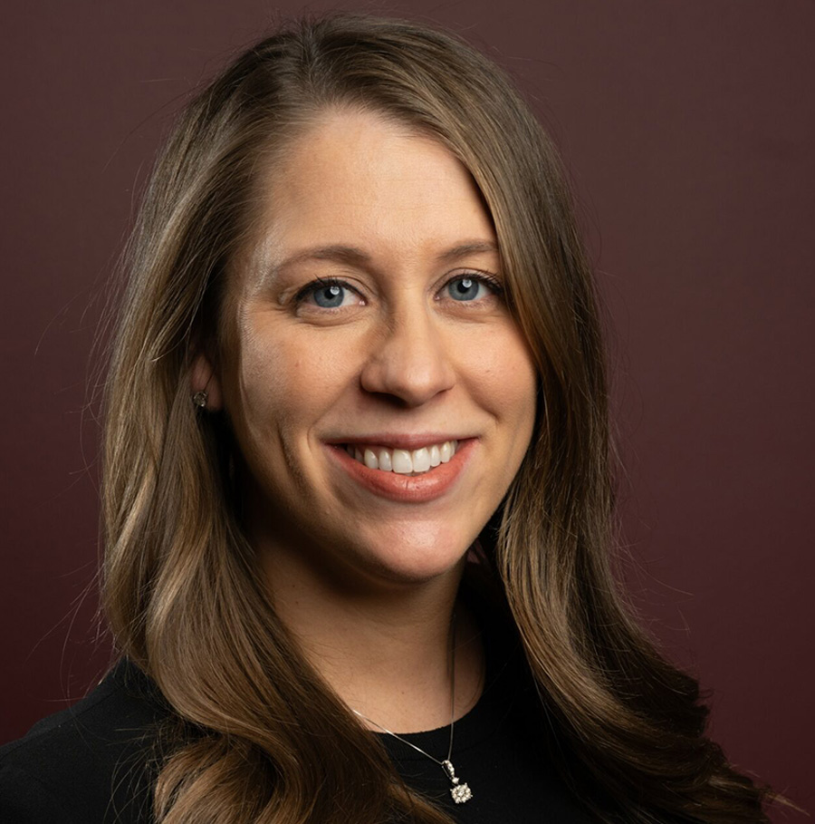 Portrait orientation close-up headshot photograph of Jenna Wright smiling in a black dress with a thin chrome necklace equipped around her