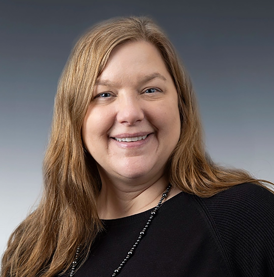 Portrait orientation close-up headshot photograph of Jennifer Segelhorst smiling in a black sweatshirt with a blacked beaded necklace equipped around her