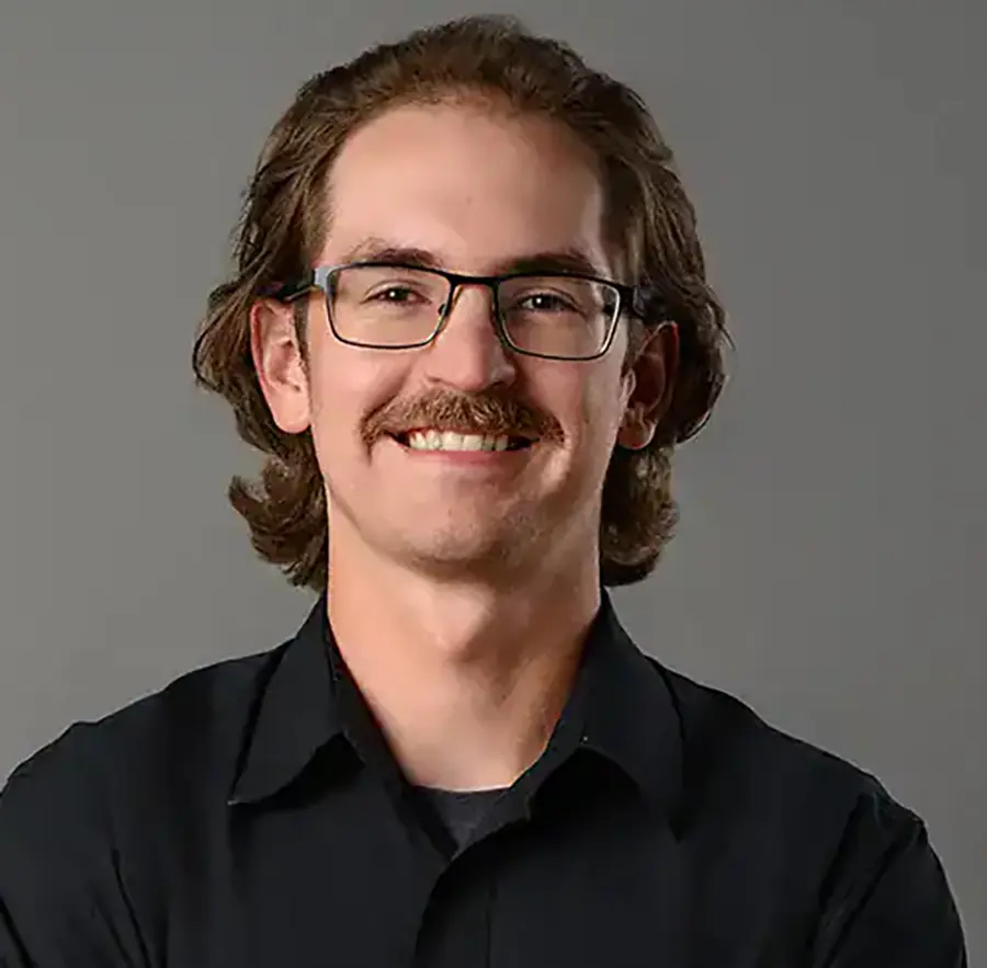 Headshot photograph of Nick Parker smiling in a black button-up dress shirt with prescription eyeglasses