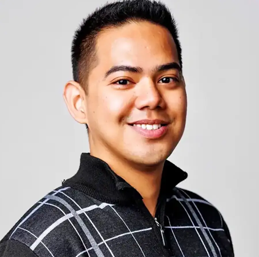 Headshot photograph of Al Asuncion smiling in a black quarter-zip sweater that has a white and grey windowpane plaid pattern