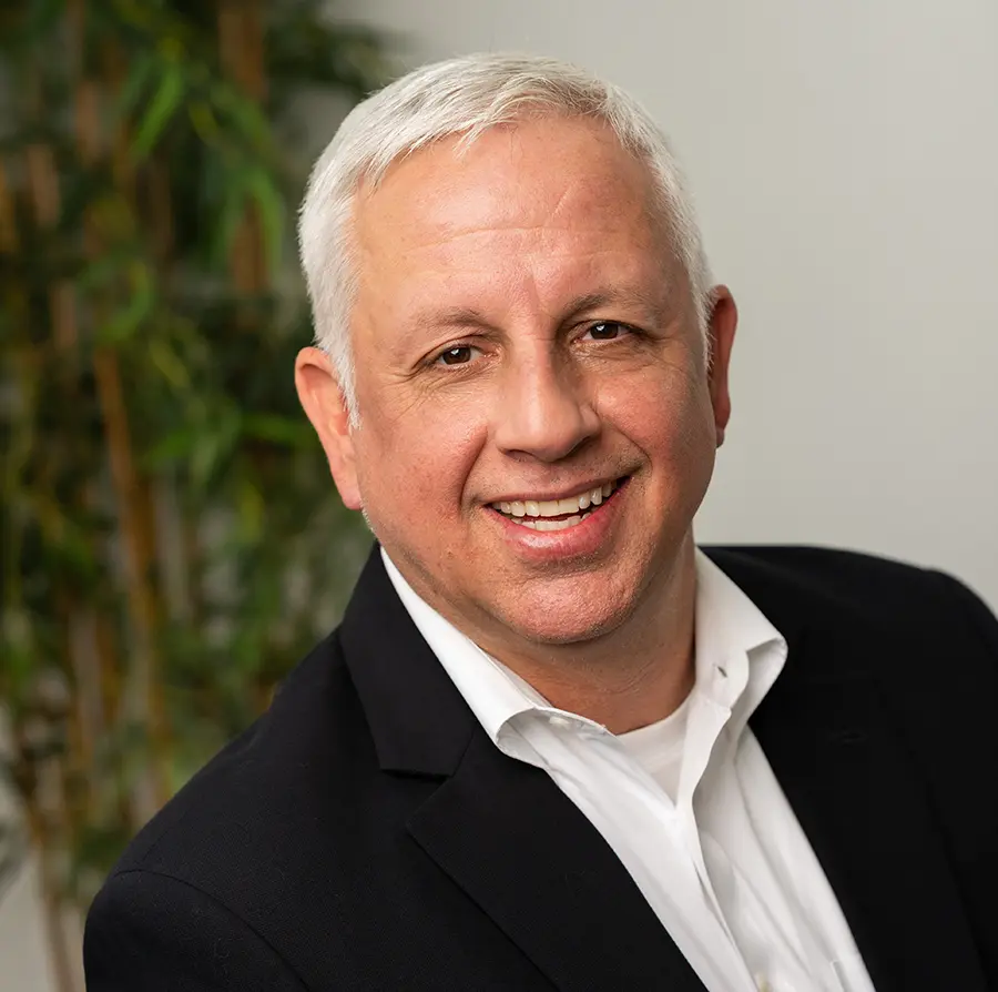 Headshot photograph of Joe Aley smiling in a black business blazer suit