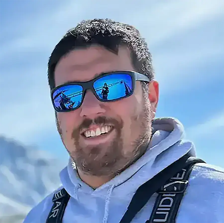Headshot photograph of Josh Miranda smiling in a white sweater and has on sunglasses